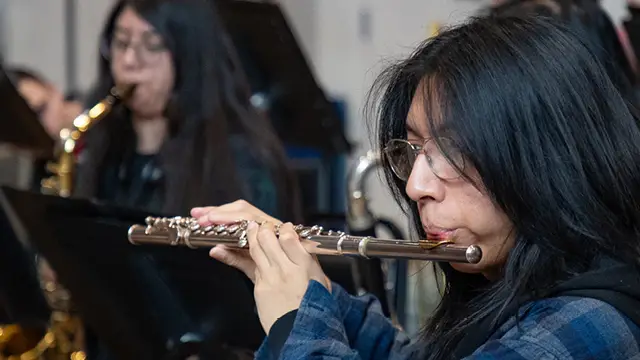 Music student playing the flute in the foreground and another student playing saxophone in the background.