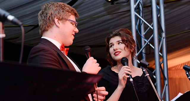 Two student performers looking at each other while singing into microphones.