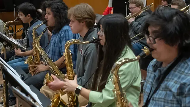 Group of music students playing together with trumpets in the back and saxophones in the front.