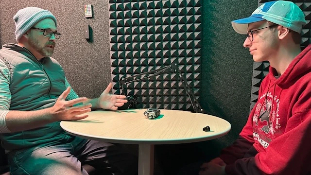 Students talk with a microphone between them in a podcast booth
