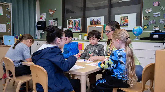 Teacher and young students color at a classroom table