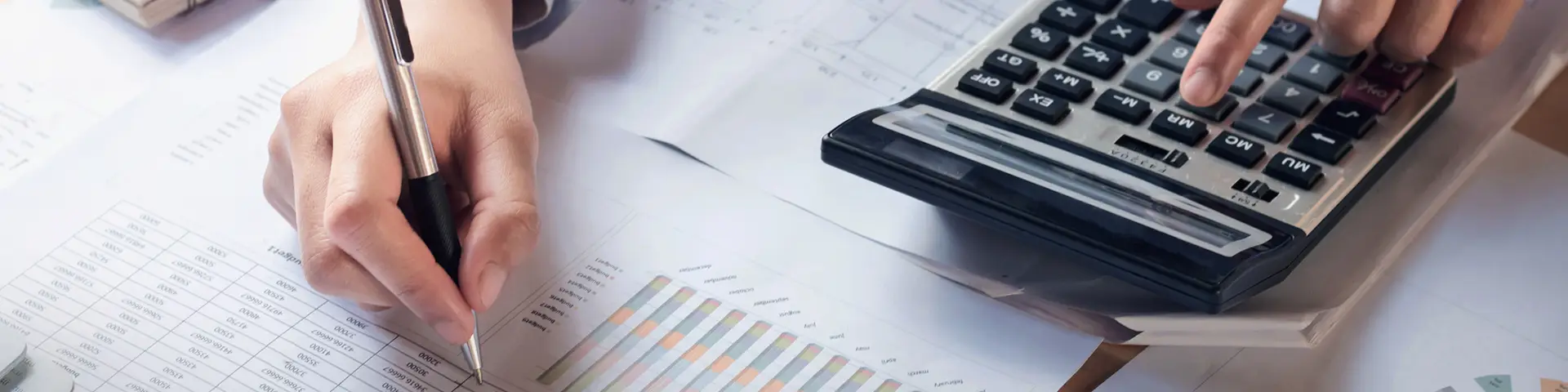 A person using a calculator on top of accounting paperwork.