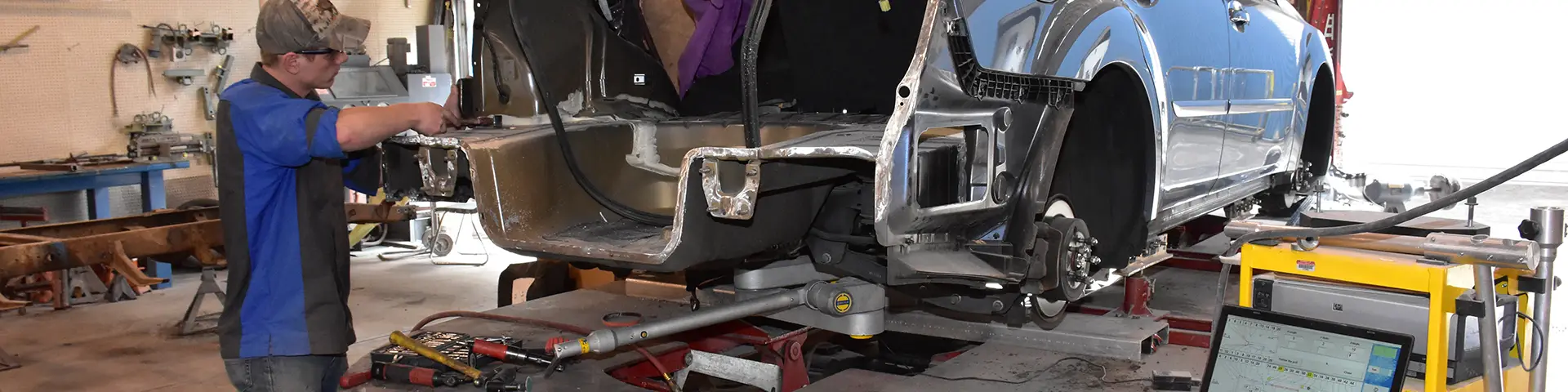 Auto technician working on a silver metal car frame.