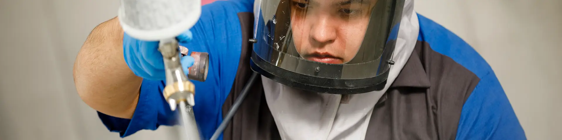 Student wearing protective face shield uses paint sprayer on car