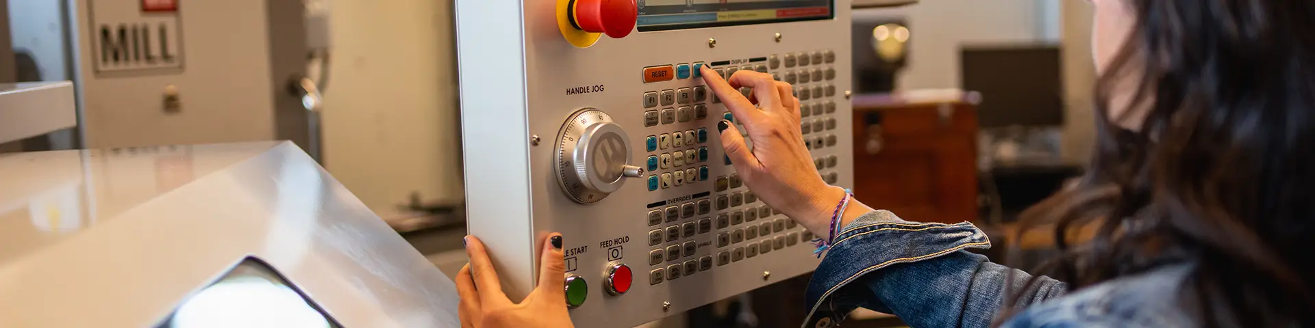 Student pushes buttons on a penel to operate computer-aided manufacturing equipment