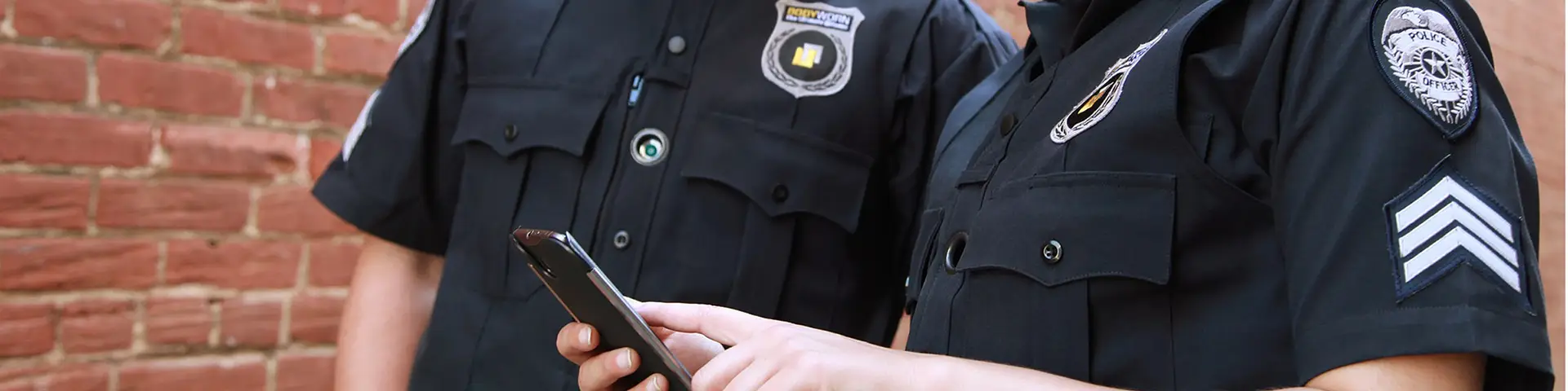 A close up of two police officers looking at a smartphone together.