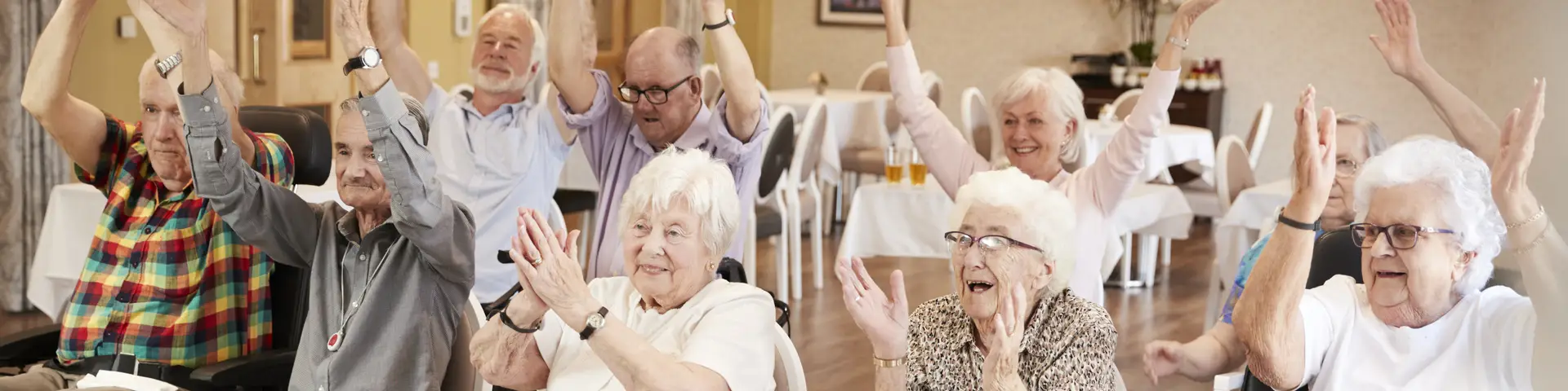 Group of elders at a senior living facility sitting in chairs and cheering on a presentation.