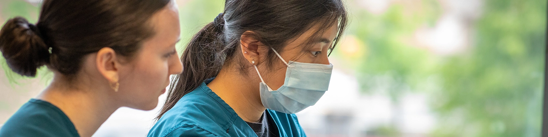 Two healthcare providers in scrubs, one wearing a surgical mask