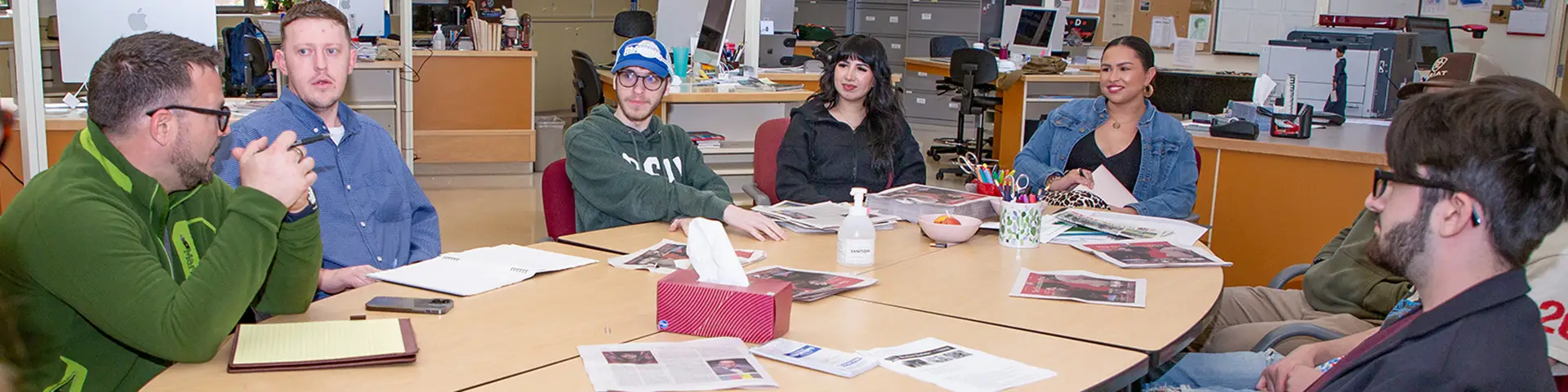 Journalism students engaged in discussion around a table with newspapers and notepads