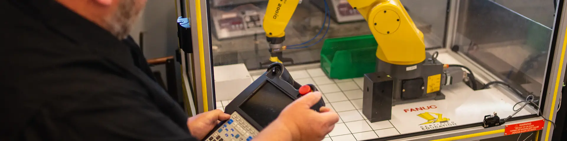 Machine operator testing a robotic arm behind a glass casing.