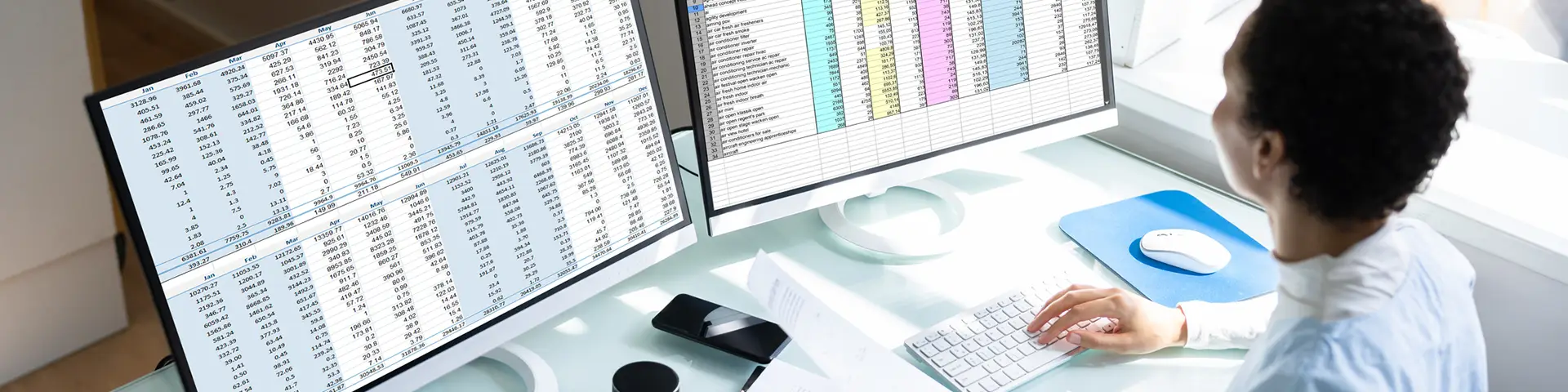 Professional reviews a spreadsheet on computer screens