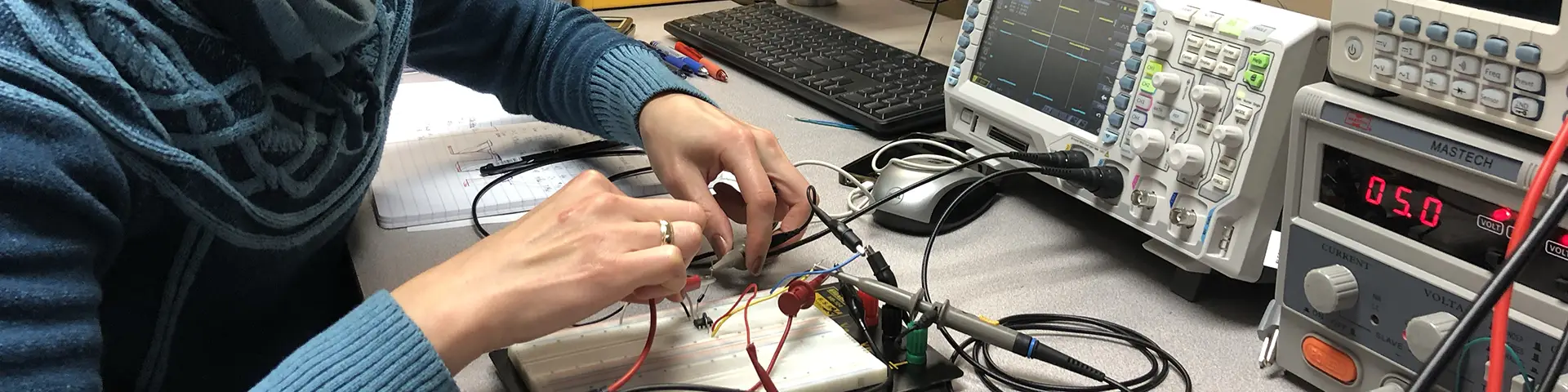 Microelectronics student working on a small circuit board full of connection points, lights and wires.