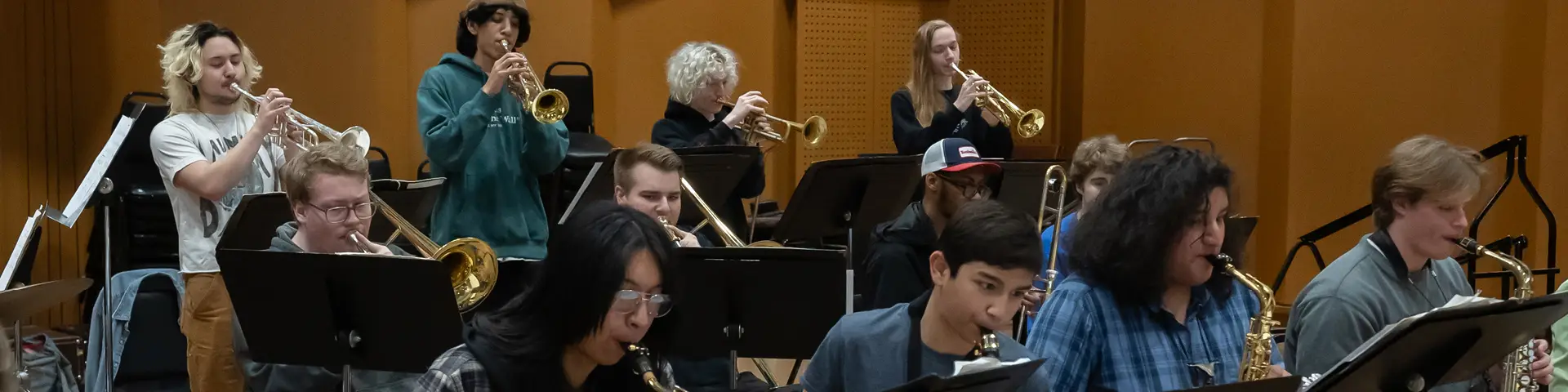 Group of music students playing together with trumpets in the back and saxophones in the front.