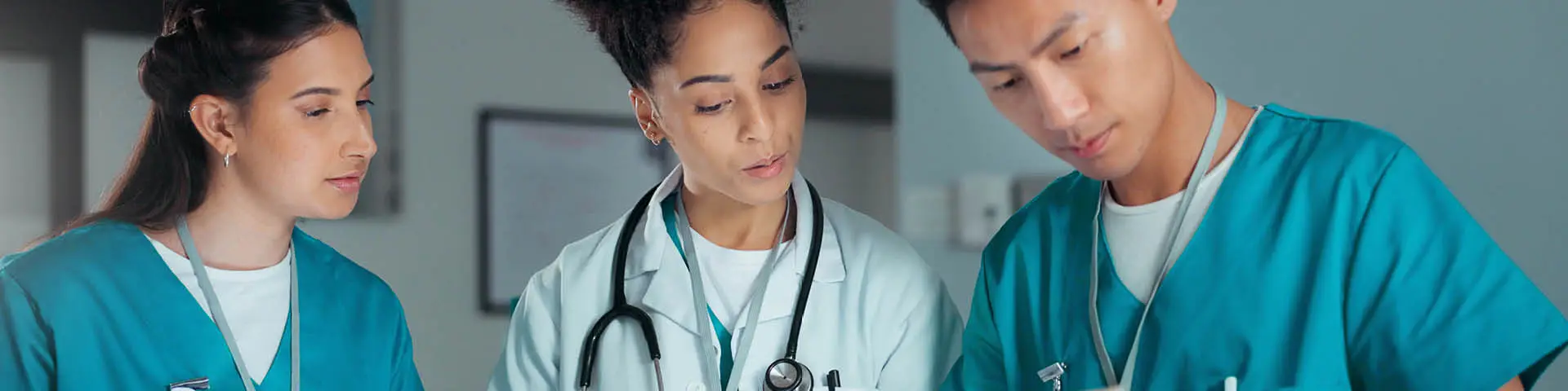 Health care provider in lab coat and stethoscope reviews documents with two other providers wearing scrubs