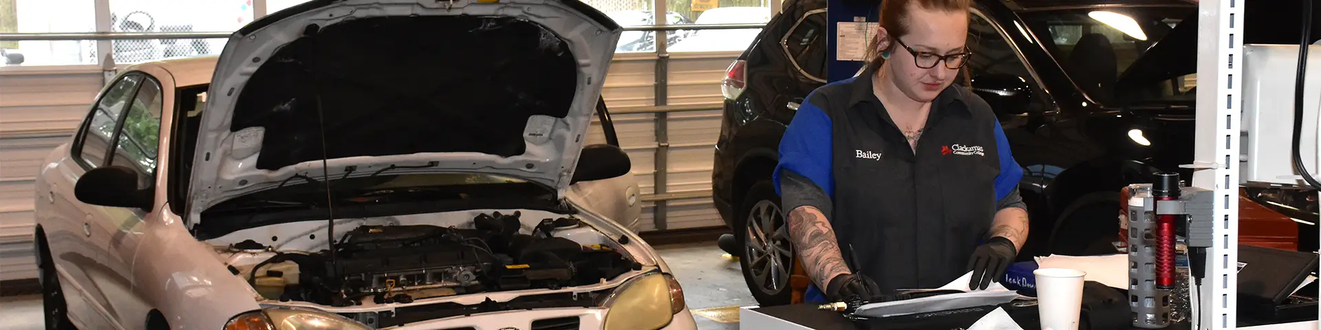 Female student in the Auto Service and Repair Lab reviewing parts and paperwork.