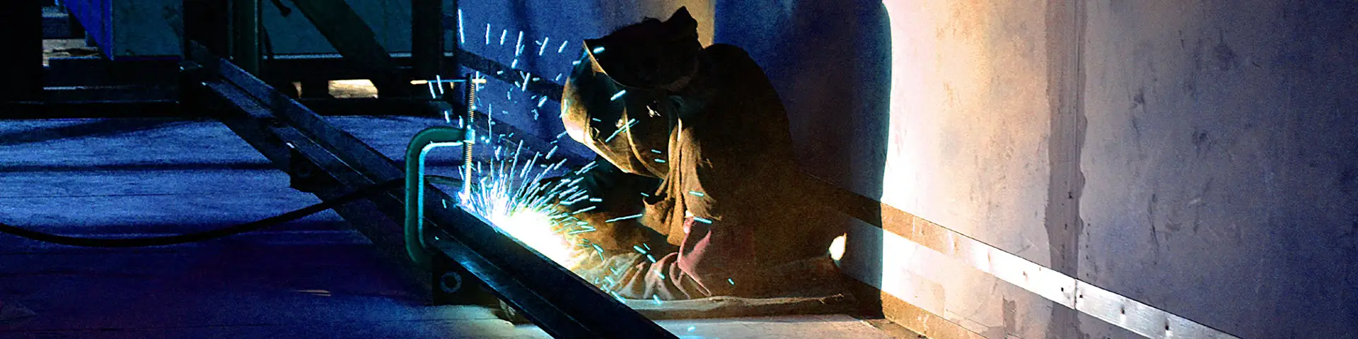 Sparks fly as welder in protective equipment does welding work on a metal beam