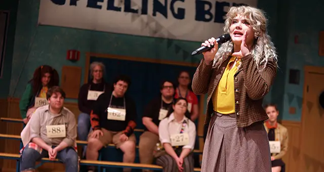 Scene from student play with student actor spotlighted on stage speaking into a microphone