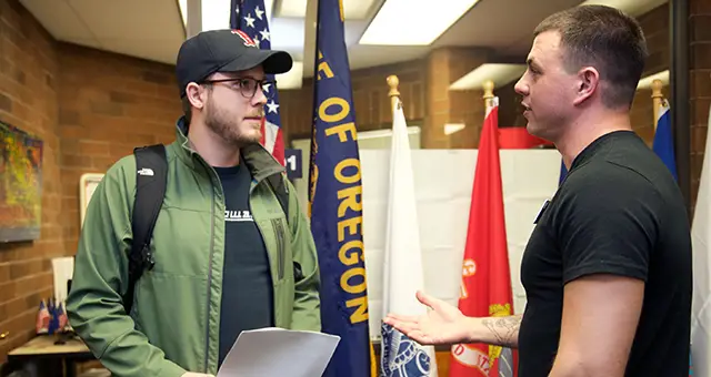 Two students talk in CCC's VET center office with flags in the background