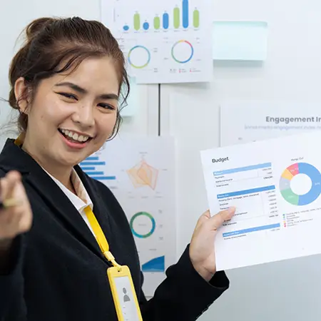 Accounting student holding up a analytics report in front of a whiteboard while fielding presentation questions.