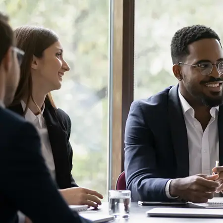 Two business professionals in formal attire speak together at a large table during a business meeting.