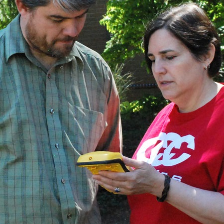 Two people are using a GIS mapping tool in a wooded outdoor setting.