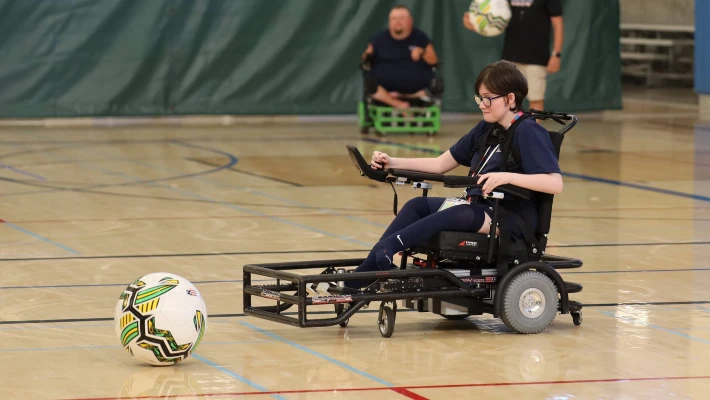 Accessible All-Stars power wheelchair user playing soccer in a gym