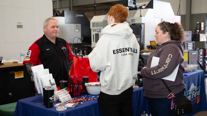 Two CTE showcase attendees talk to a CCC automotive instructor at a booth 