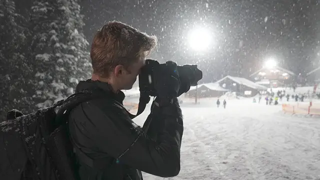 Student photojournalist looks into the camera viewfinder on a snowy evening on Mount Hood