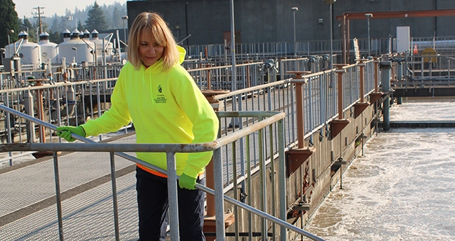Wastewater operator and CCC alum Victoria Mendez extends a tool into the water in a wastewater facility